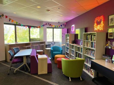 Pride Center Cultural Community Center has colorful couches and chairs with a study area, relaxing area, and tv for entertainment.