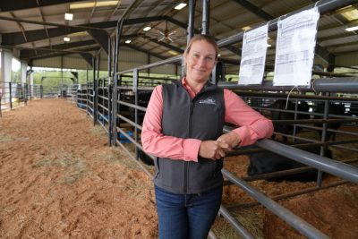 A smiling woman leans against a rail inside a large livestock barn.